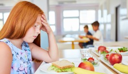 Niña triste delante de un plato en un comedor escolar